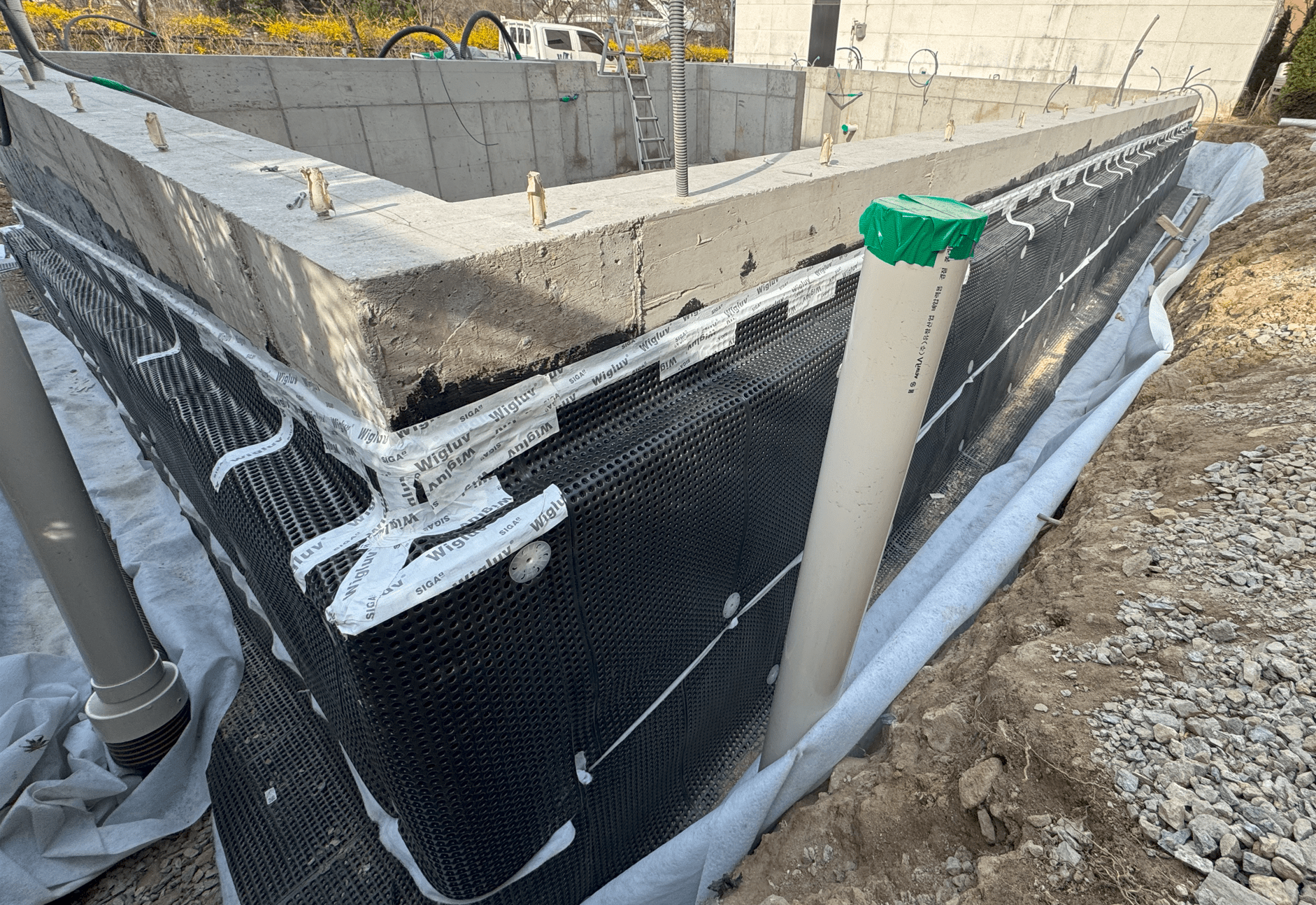 기초 구조물 주변에 방수 보호층이 설치된 모습, 드레인 파이프가 보이며, 기초 벽체의 외부가 보호재로 감싸져 있음.