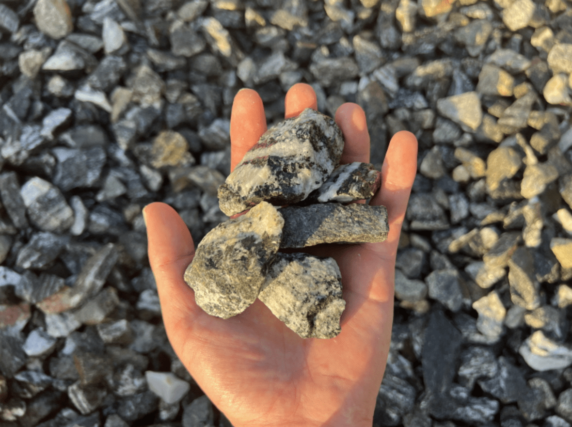 A hand holding several pieces of crushed stone with a backdrop of more crushed stones.