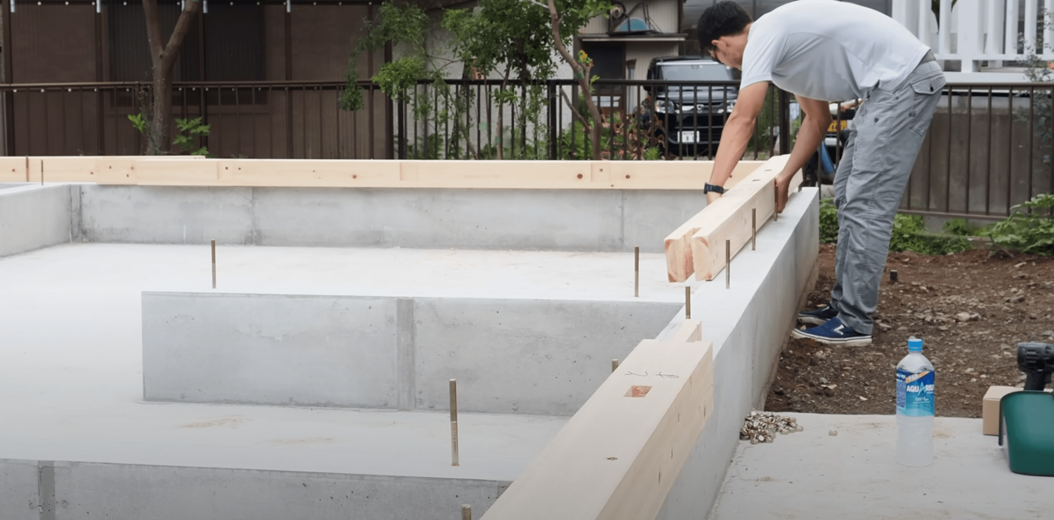 구조물의 기초를 조립하는 작업을 진행 중인 남성, 바닥에 나무 기둥을 놓고 있는 모습.