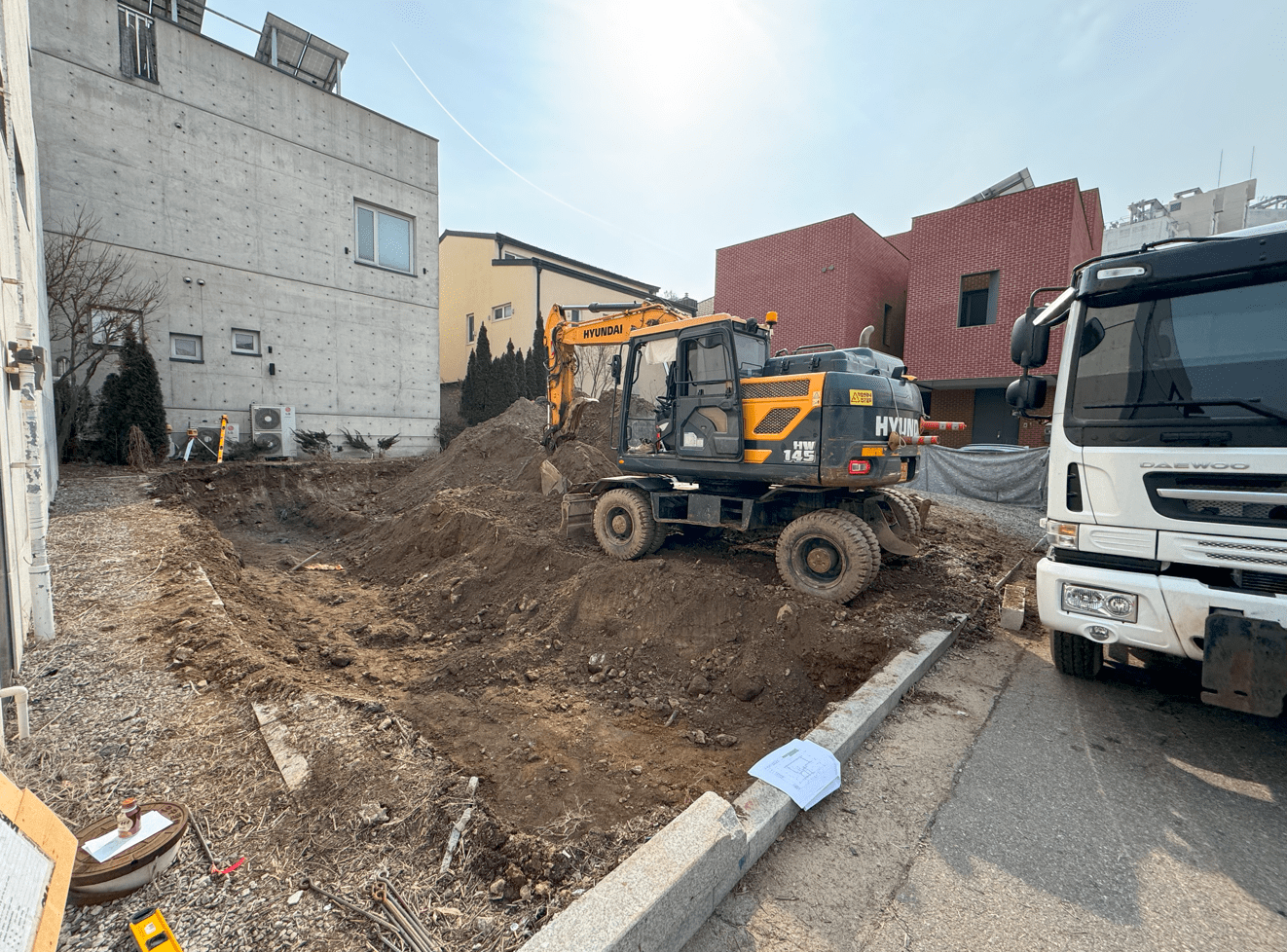 건설 현장의 굴삭기와 토사가 쌓인 모습. 주변에 여러 건물과 도로가 보임.
