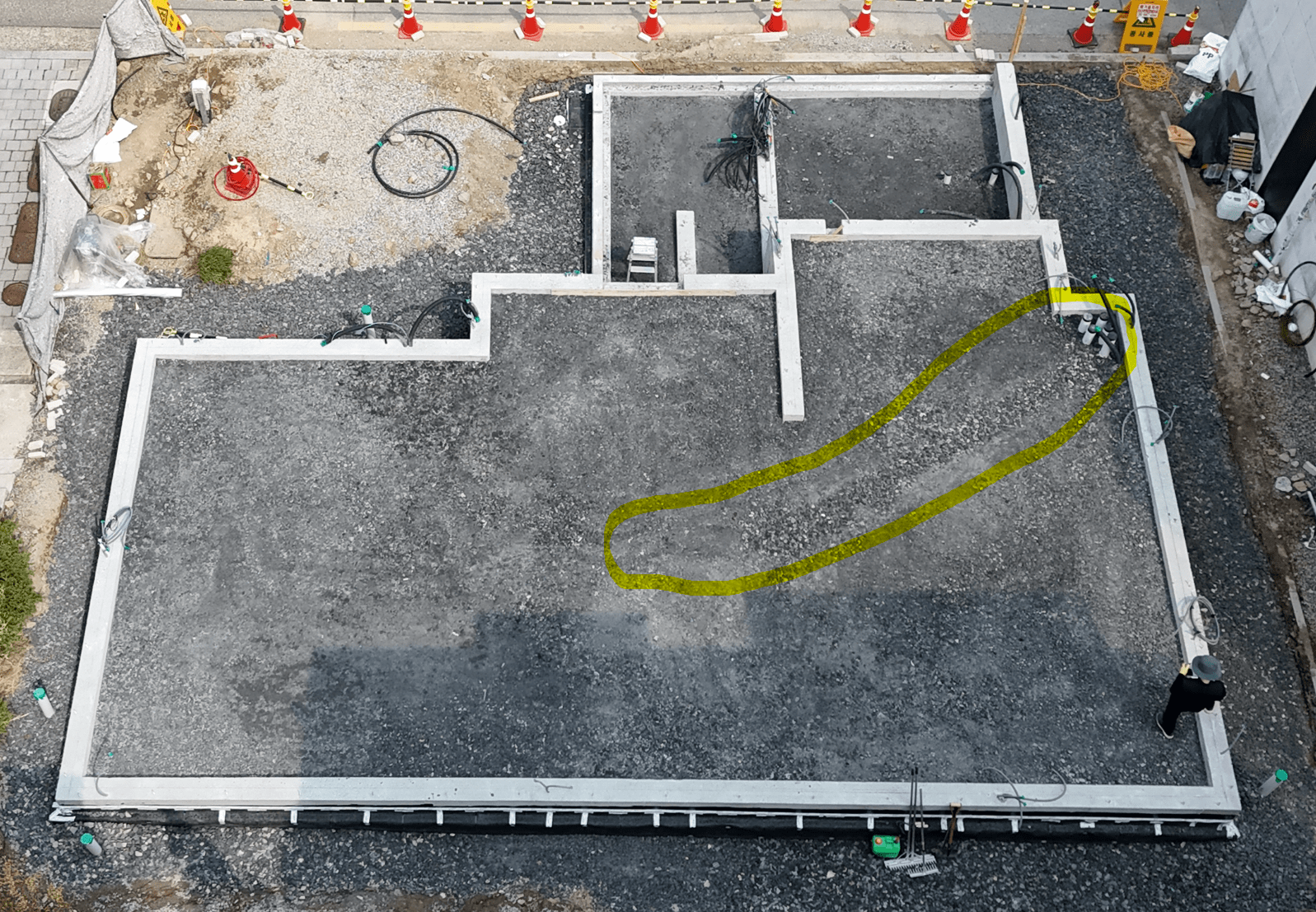 상부에서 촬영한 건물 기초 작업 현장, 폼그라스 골재로 채워진 바닥과 기초 벽 구조가 보임. 노란 선으로 표시된 부분은 라돈가스 배출용 PVC 파이프가 매립된 위치.