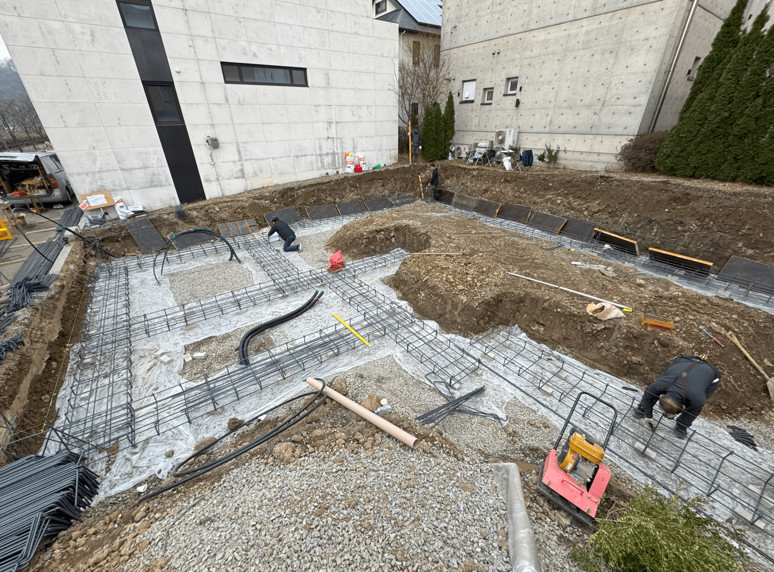 공사 현장에서 줄기초를 준비하는 모습, 철근과 자재가 배치되어 있으며 작업자들이 작업 중인 장면.