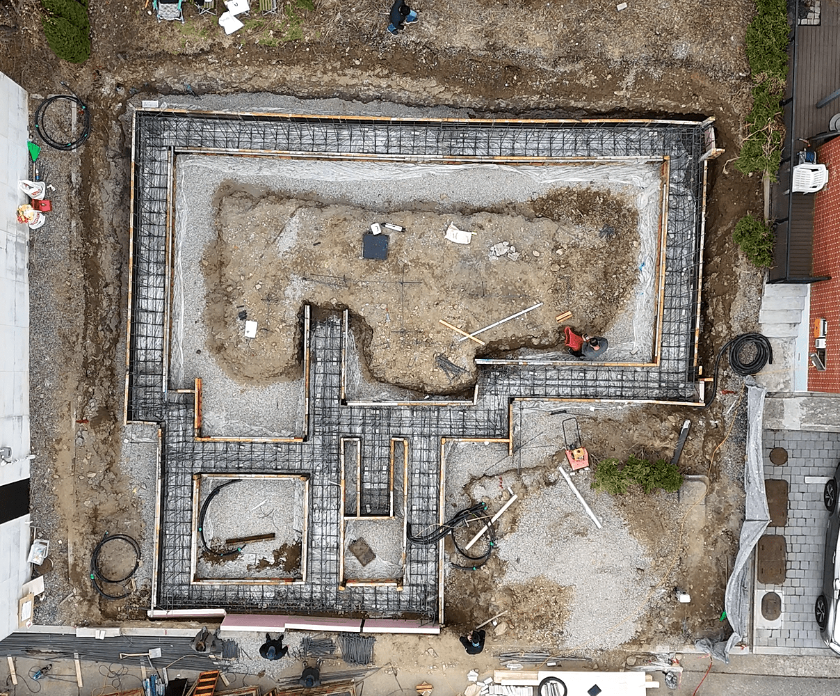 차량이 주차된 주택 공사 현장, 줄기초를 위한 콘크리트 블록이 설치되어 있으며, 주변에 작업자와 장비가 보입니다.