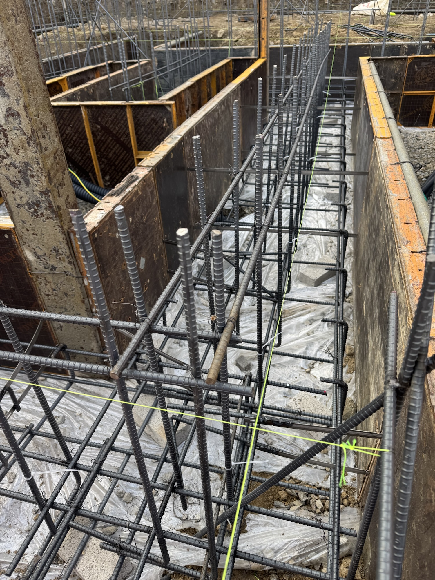 철근 구조물 위에 비닐이 깔려 있는 줄기초 푸터 시공 현장 이미지