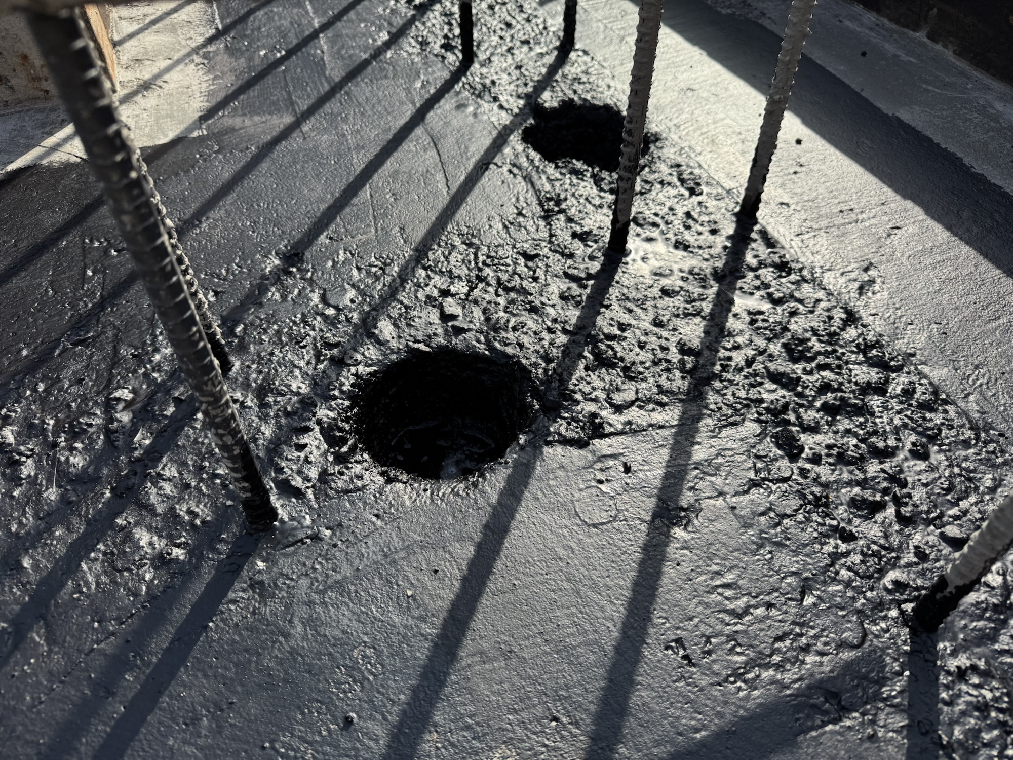 콘크리트 푸터 위에 규칙적으로 배열된 철근과 공사 후 남은 콘크리트 표면의 모습, 바닥에 구멍이 있는 구조.