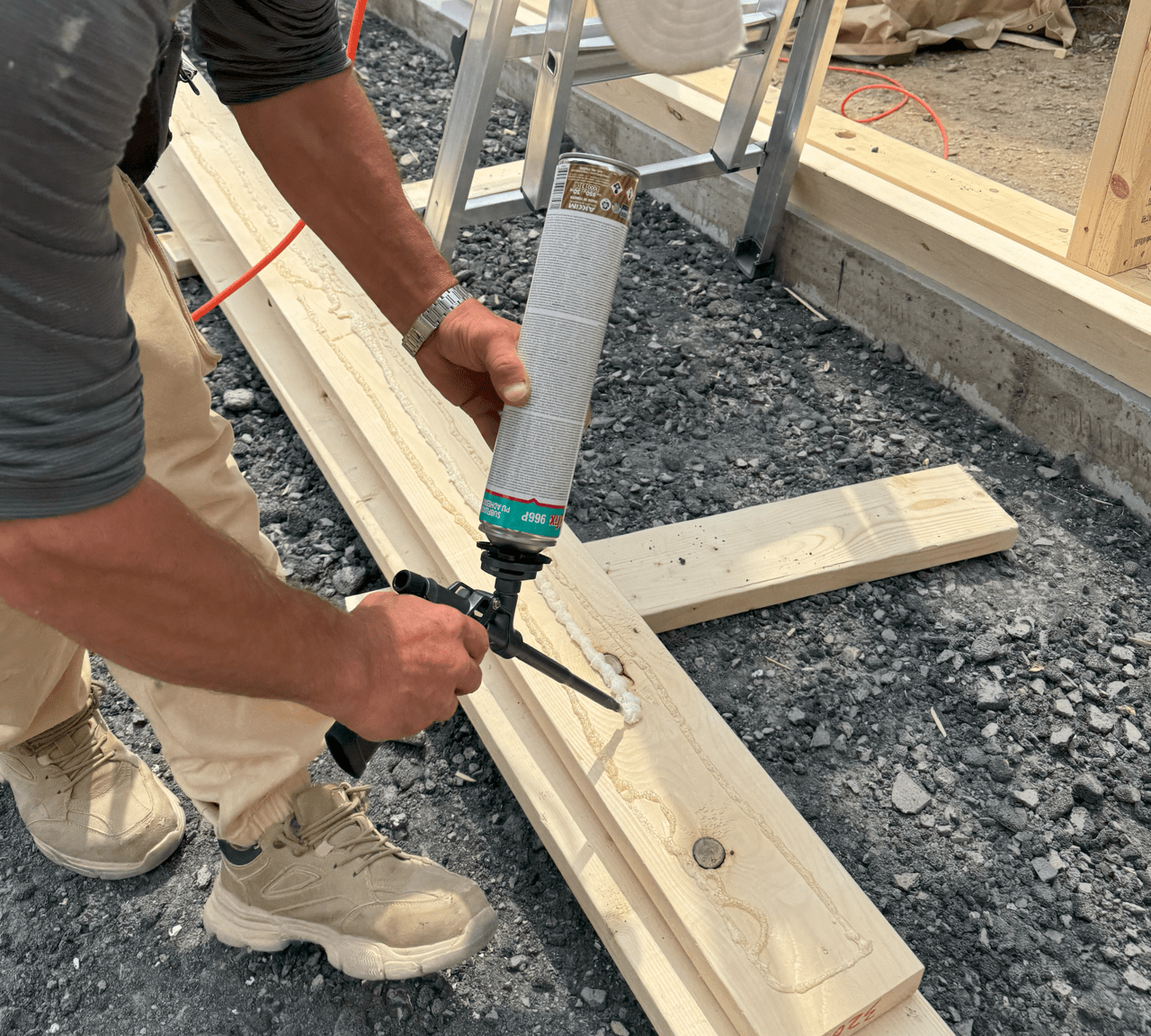 목재 빔에 구조용 접착제를 바르는 작업자. 접착제를 포함한 건축 자재가 배경에 보인다.