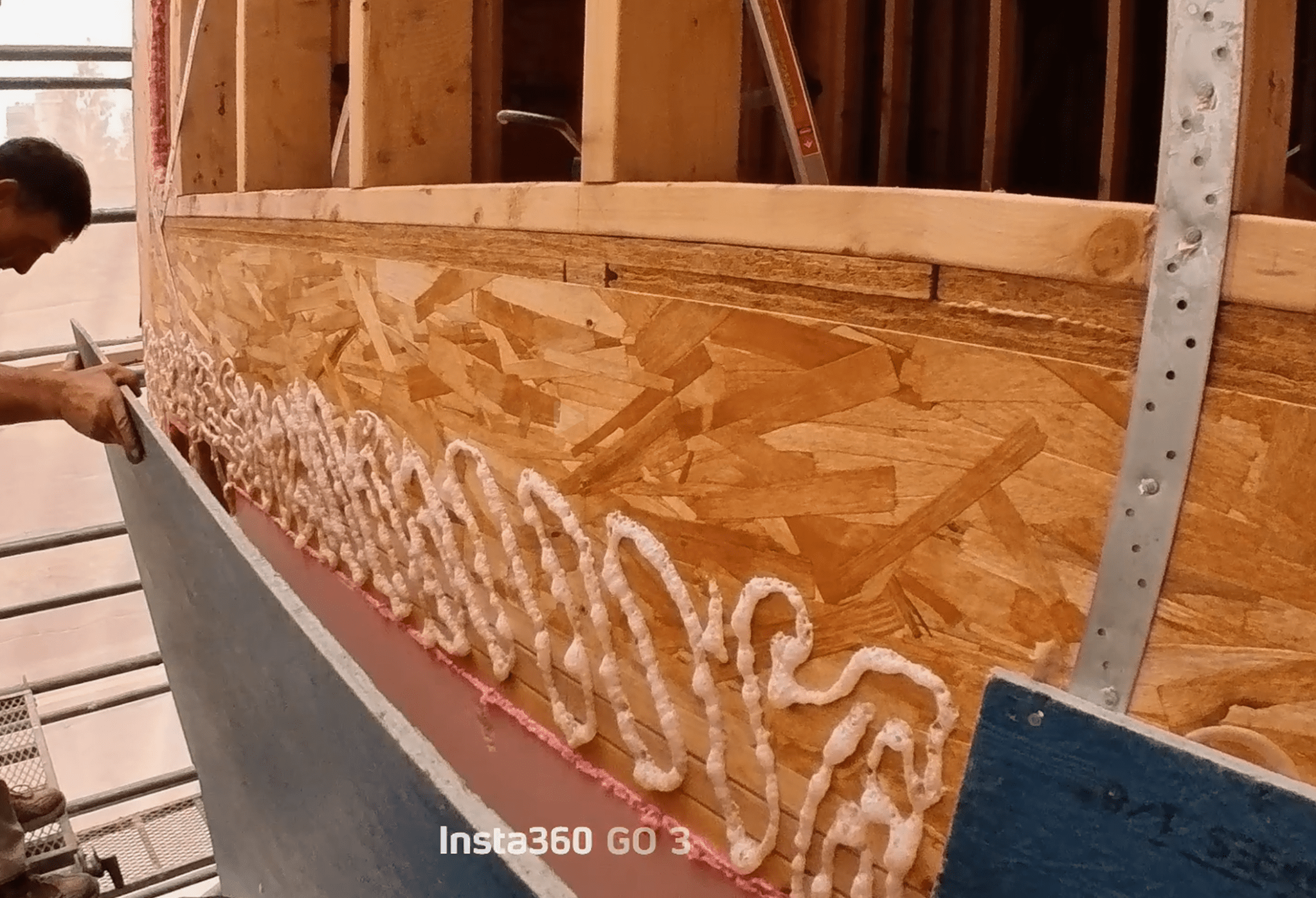 목조 구조물에 접착제를 사용하여 합판을 부착하는 모습. 작업자가 접착제를 바르고 있는 장면.