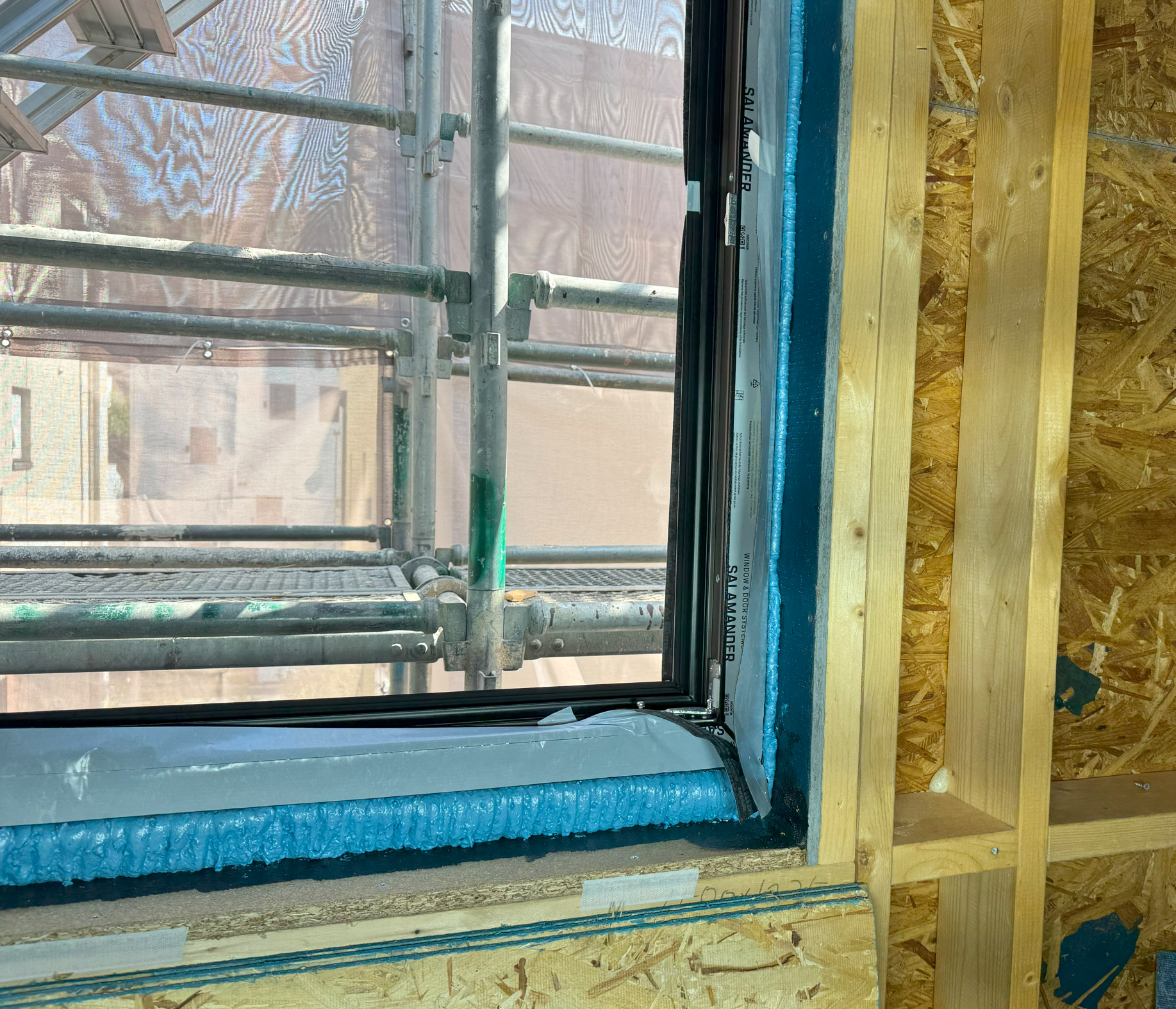 창호 설치 과정에서의 내부 모습, 외부 scaffolding와 절연재가 보이는 창호 주위의 구조.