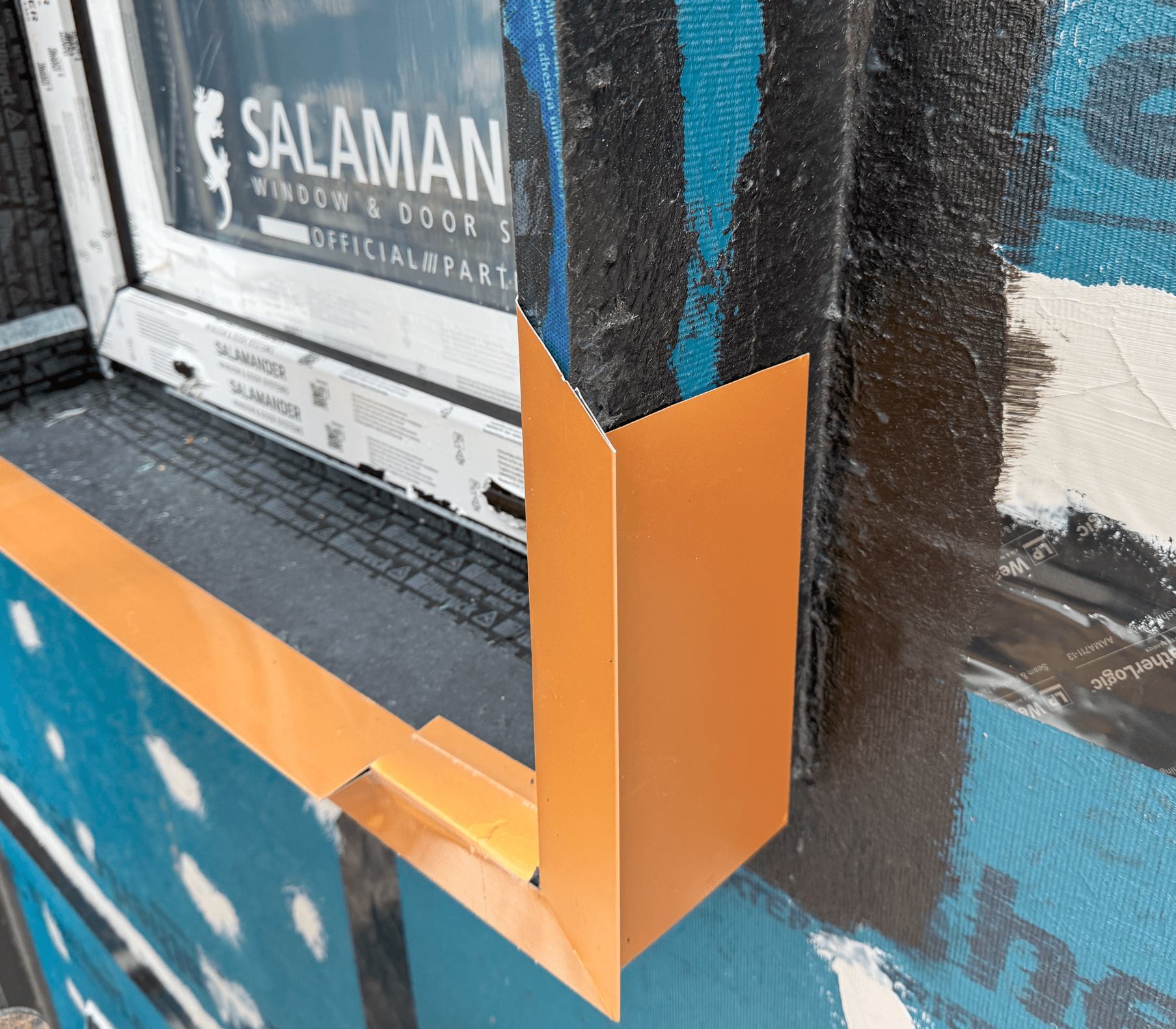 Close-up view of a window corner showing the copper flashing detail installed around a Salamander window frame, with surrounding construction materials visible.