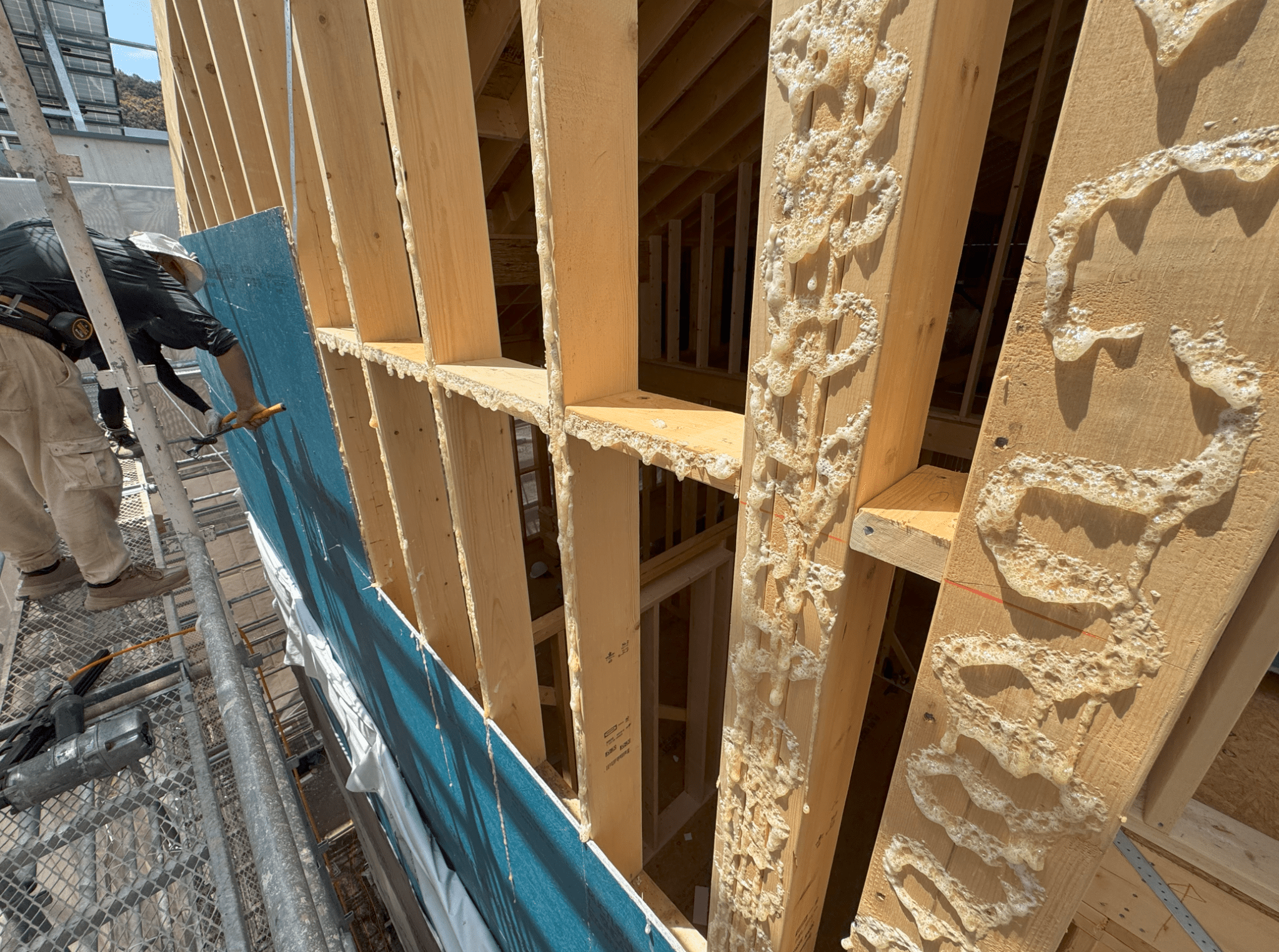 A construction worker applying insulation foam between wooden framing during house construction.