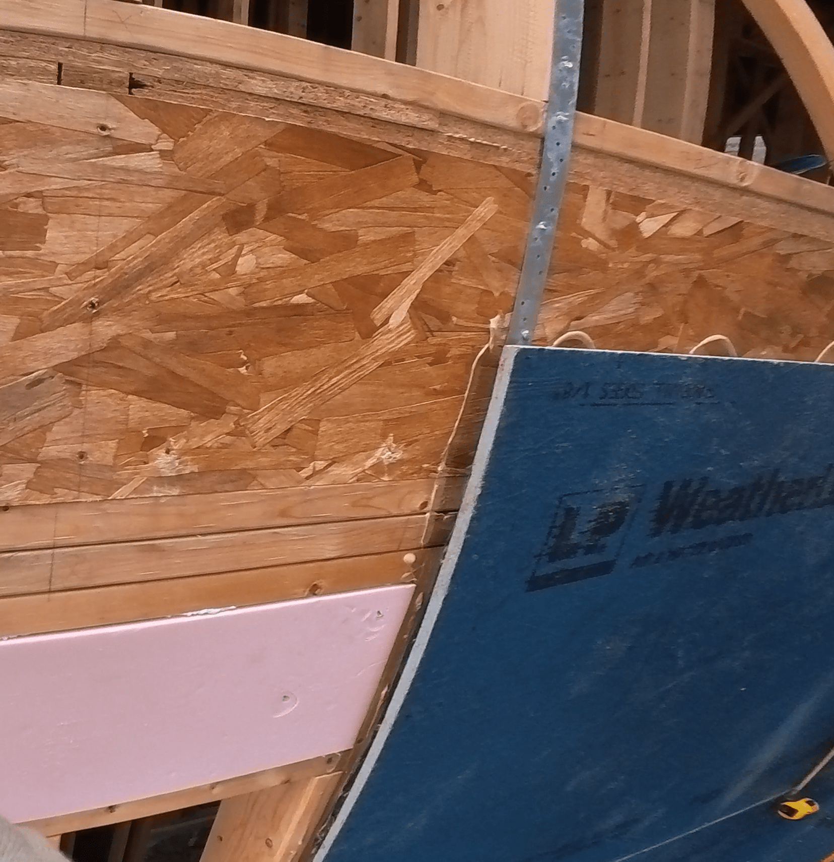 건축 자재가 부착된 벽의 근접 사진으로, 나무 패널과 방수판이 함께 사용되고 있는 모습입니다.