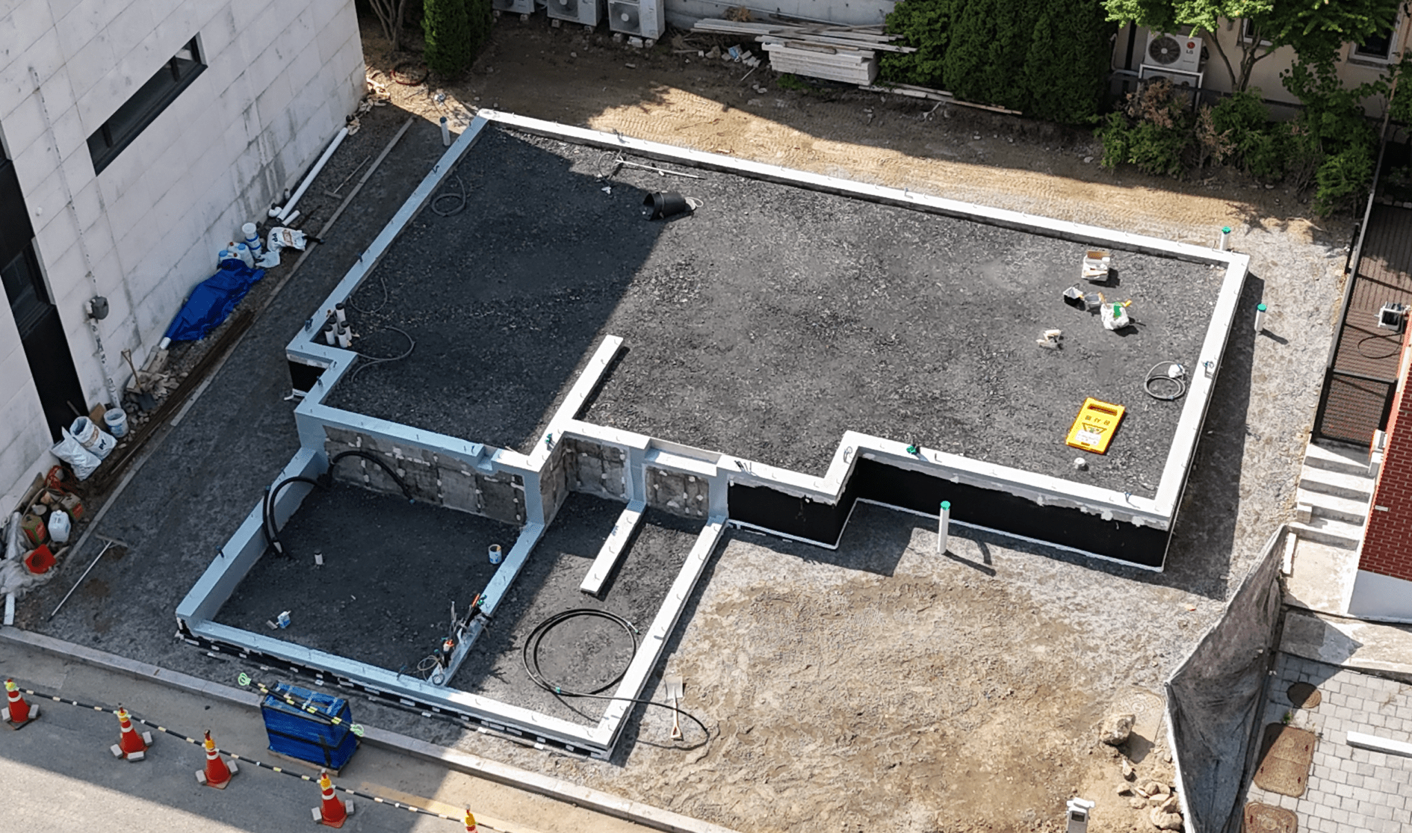 Aerial view of a construction site with a foundation laid out for a building, featuring a gravel base surrounded by walls, tools, and construction materials.