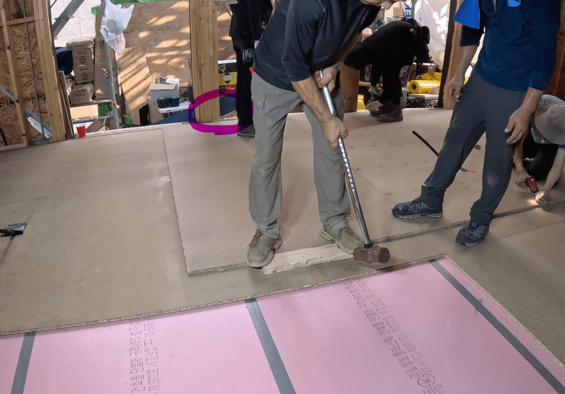 Construction workers installing plywood flooring over insulation in a home under construction.
