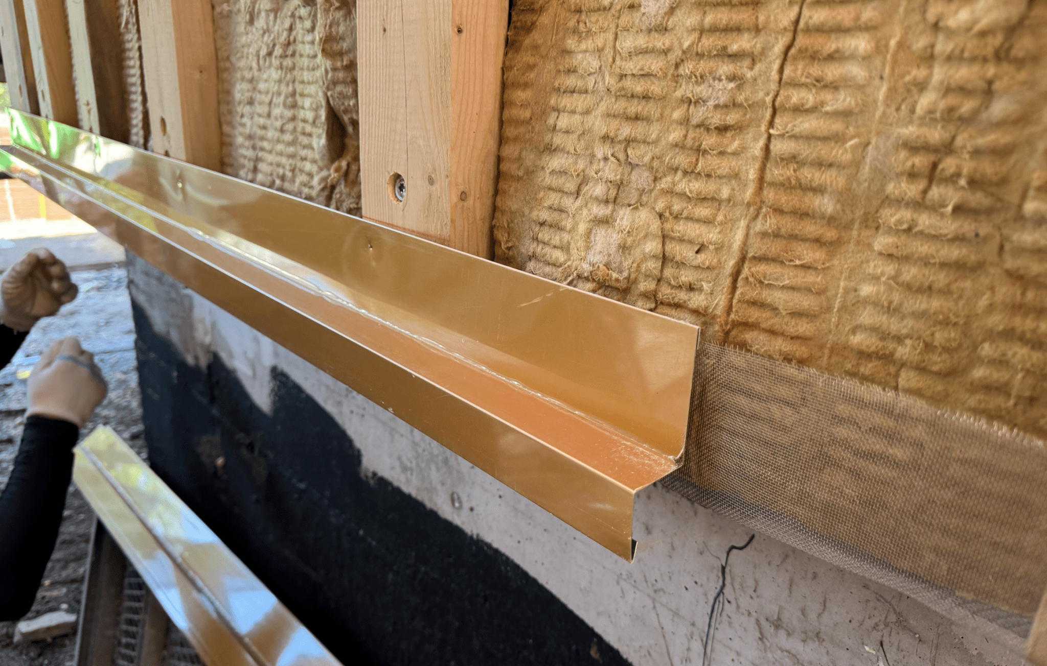 금속 재질의 빗물받이 시스템이 설치되고 있는 모습. 벽면이 치장용 단열재로 보강되어 있으며, 방수 기능을 강화하기 위한 검은색 코팅이 보인다.