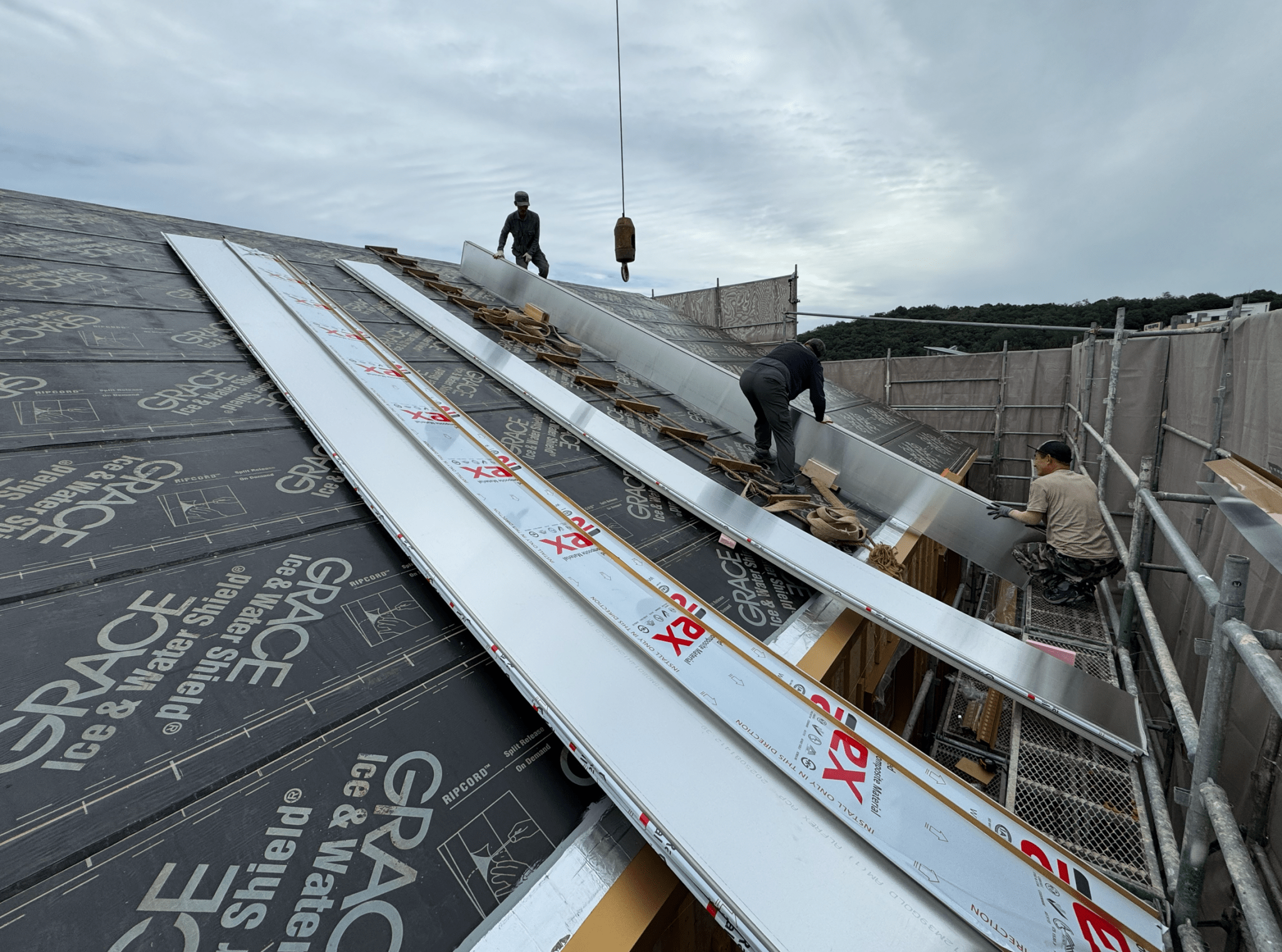 건물 지붕 위에서 작업하는 인부들이 방수막과 지붕 패널을 설치하고 있는 모습
