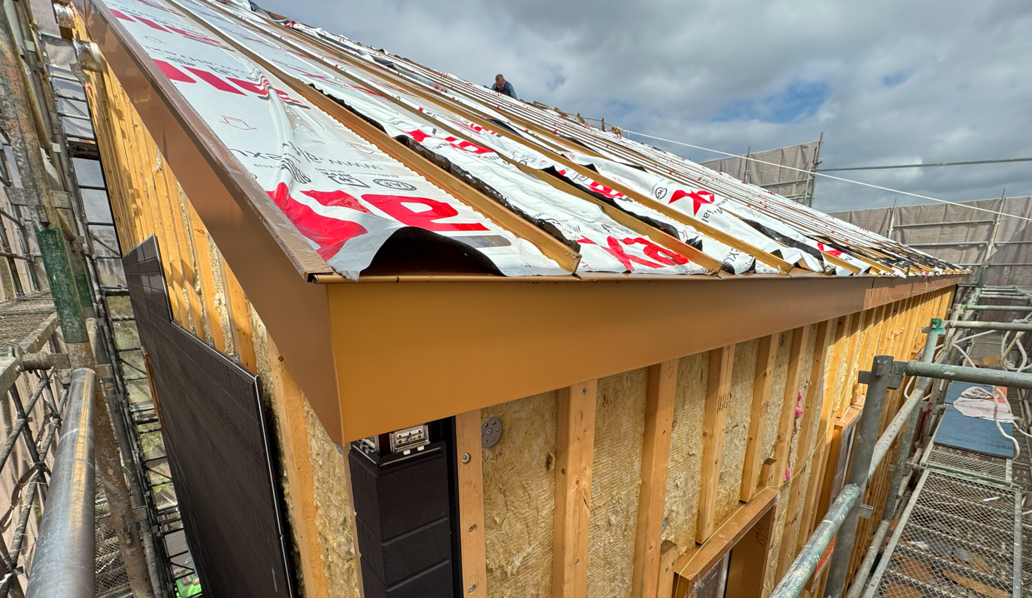 지붕의 일부분과 작업 중인 사람의 모습이 보이는 집의 외관. 지붕에는 방수 시트가 깔려 있고, 건물 구조물이 드러나 있다.