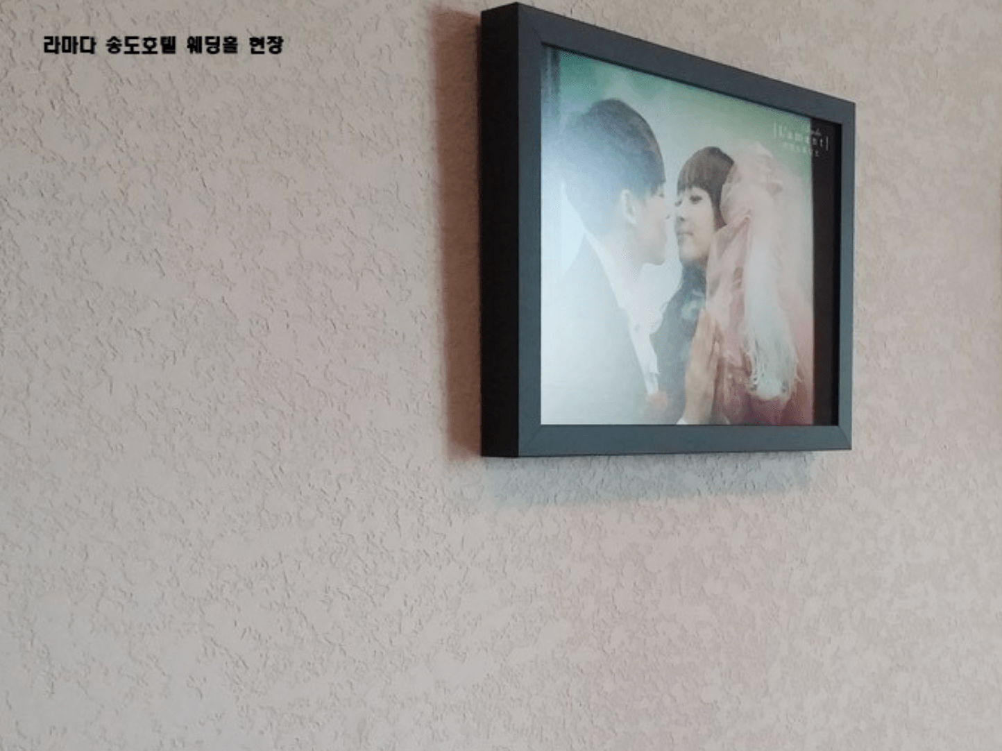 벽에 걸린 사진틀에 담긴 커플이 서로 사랑스러운 눈빛을 교환하고 있는 모습.